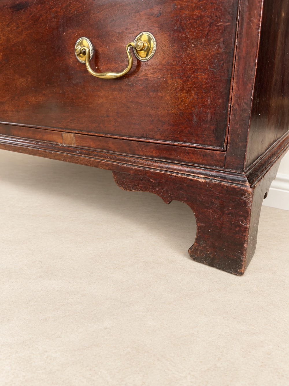 A Georgian mahogany chest of drawers featuring two short drawers above three long drawers with brass swan-neck handles, raised on bracket feet. View VII