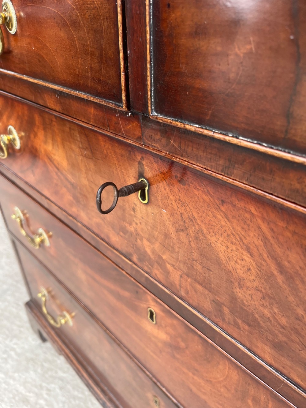 A Georgian mahogany chest of drawers featuring two short drawers above three long drawers with brass swan-neck handles, raised on bracket feet. View IX