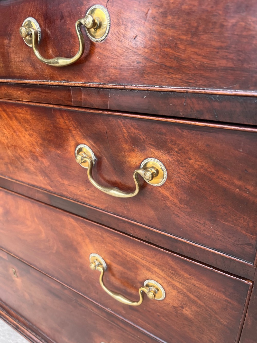 A Georgian mahogany chest of drawers featuring two short drawers above three long drawers with brass swan-neck handles, raised on bracket feet. View X