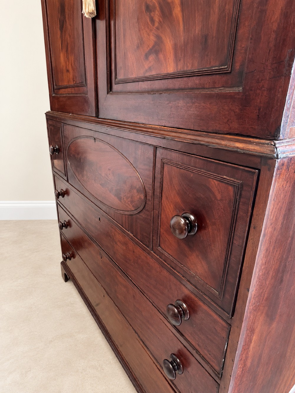 An antique Georgian mahogany linen press featuring an arched pediment, twin cupboard doors with flame mahogany panels, and a base chest with multiple drawers. View V