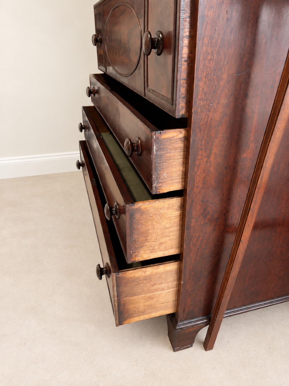 An antique Georgian mahogany linen press featuring an arched pediment, twin cupboard doors with flame mahogany panels, and a base chest with multiple drawers. View VII