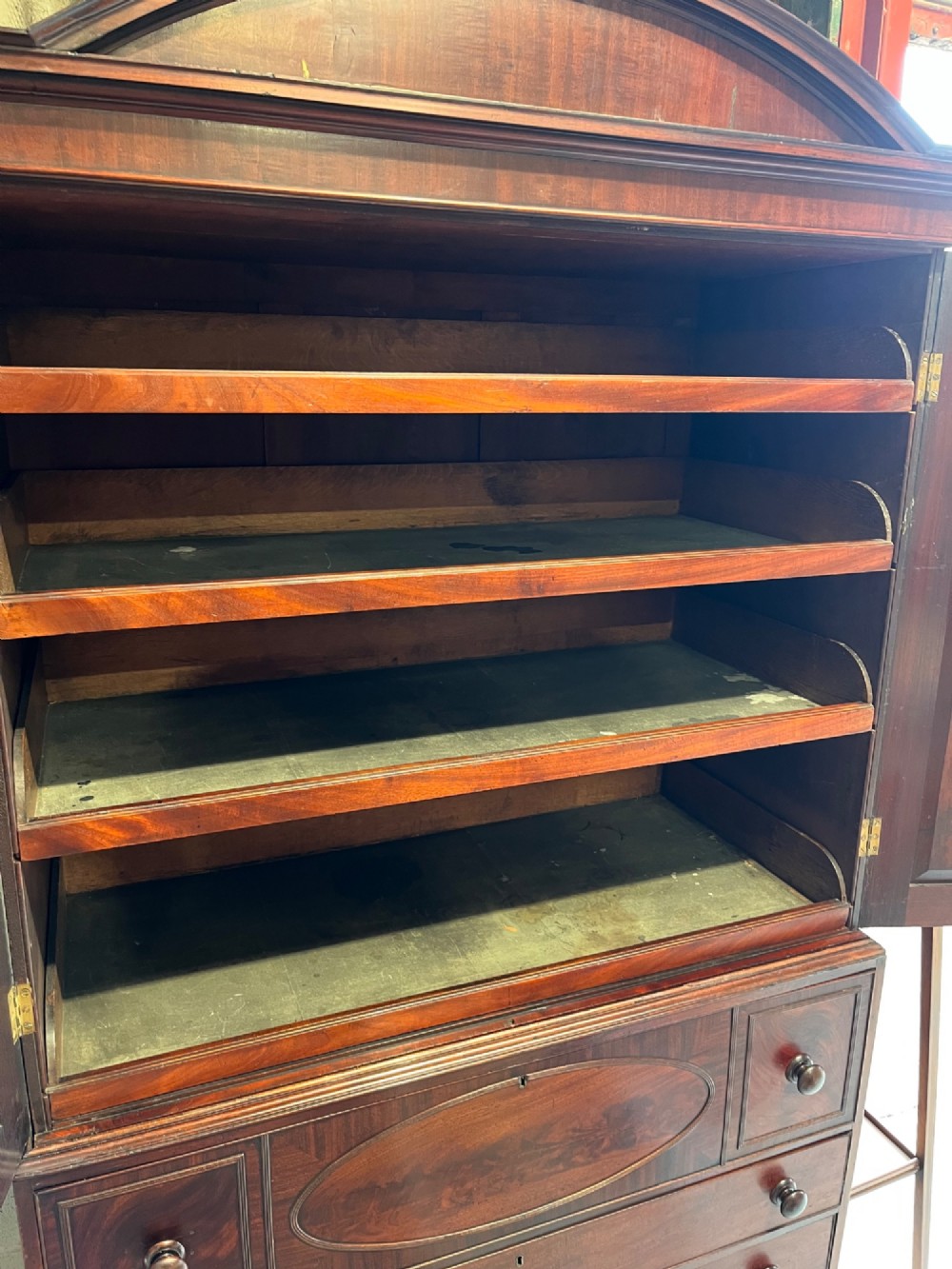 An antique Georgian mahogany linen press featuring an arched pediment, twin cupboard doors with flame mahogany panels, and a base chest with multiple drawers. View VIII