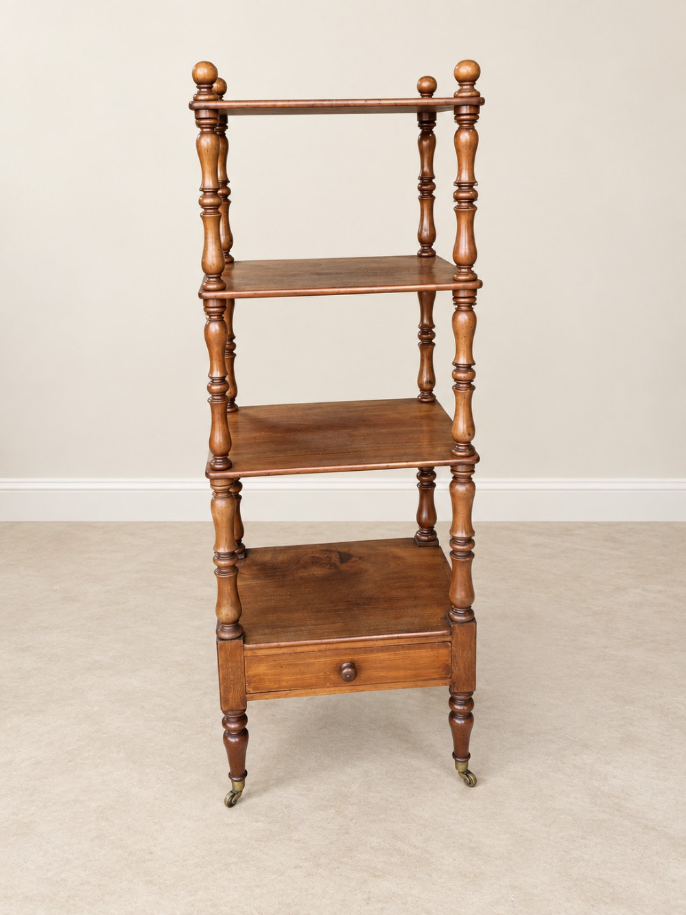A nineteenth-century mahogany four-tier what-not stand with turned column supports, top finials, a bottom drawer, and brass castors. View III