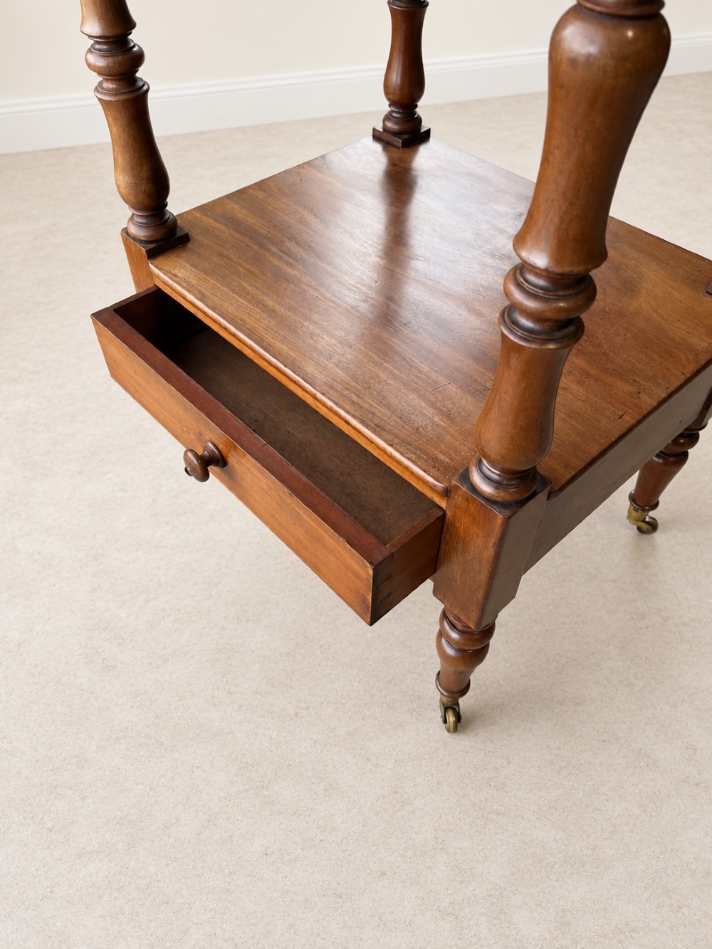 A nineteenth-century mahogany four-tier what-not stand with turned column supports, top finials, a bottom drawer, and brass castors. View VI
