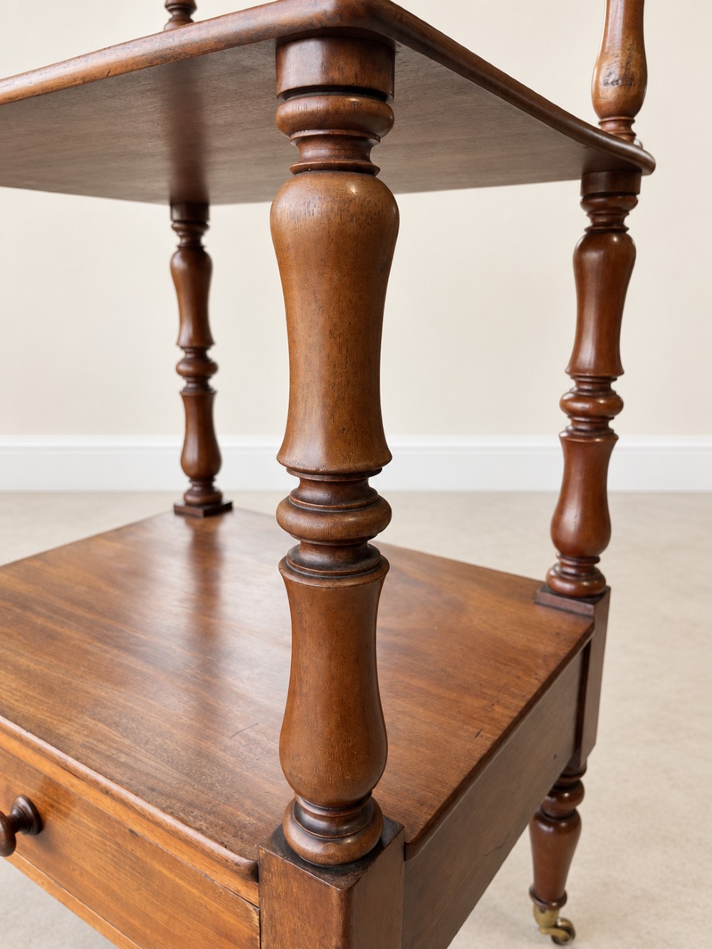 A nineteenth-century mahogany four-tier what-not stand with turned column supports, top finials, a bottom drawer, and brass castors. View VII
