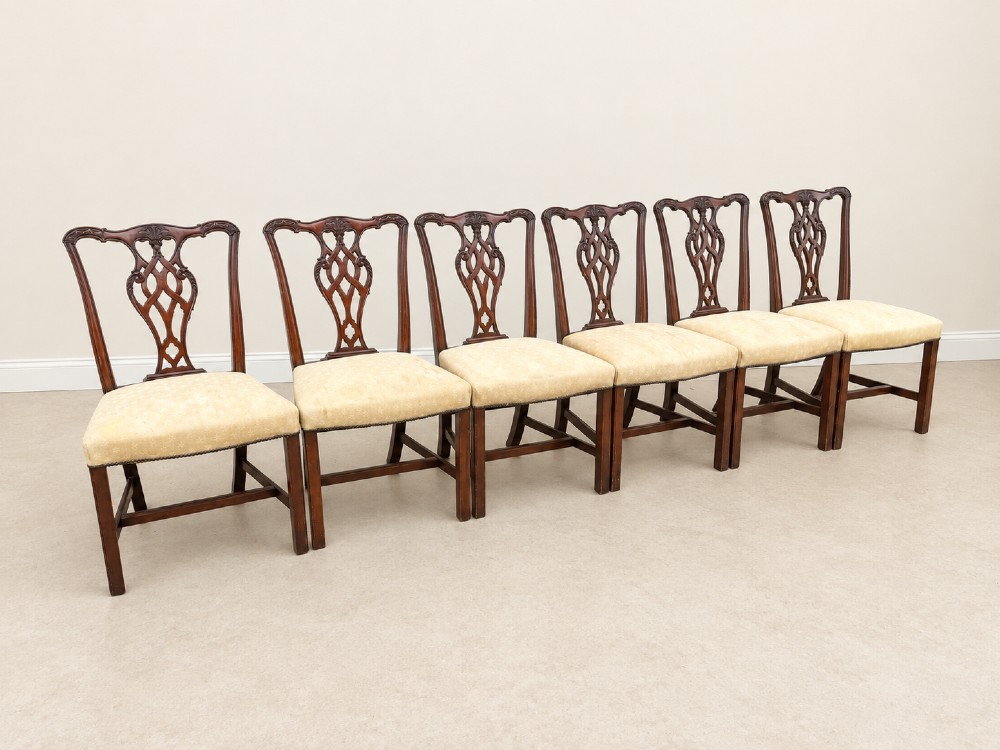 A set of six Chippendale style mahogany dining chairs featuring intricately carved pierced back splats and cream upholstered seats.