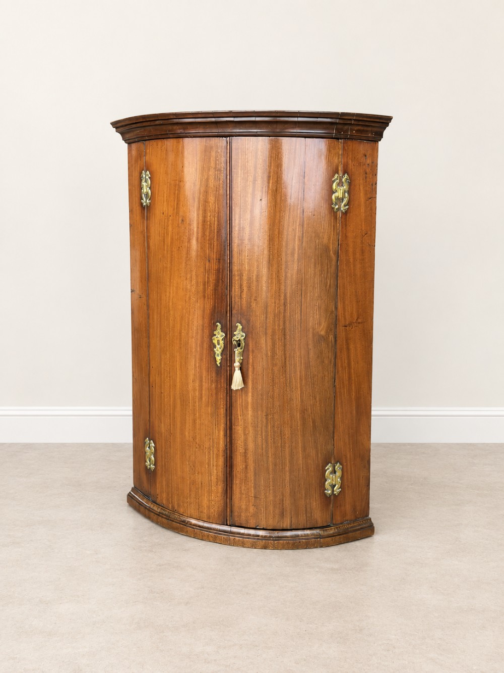 An antique Georgian mahogany corner cupboard featuring a curved bowfront double-door structure with ornate brass hinges and moulding. View IV