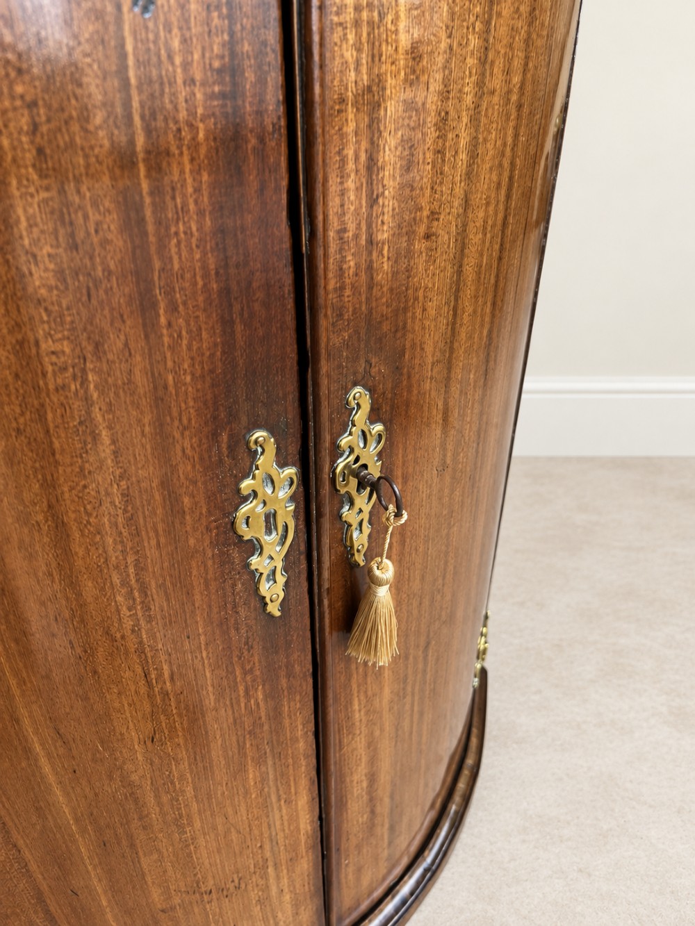 An antique Georgian mahogany corner cupboard featuring a curved bowfront double-door structure with ornate brass hinges and moulding. View VI