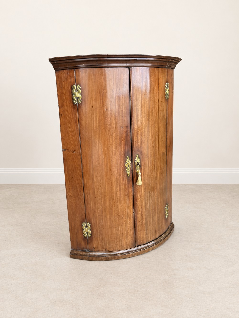 An antique Georgian mahogany corner cupboard featuring a curved bowfront double-door structure with ornate brass hinges and moulding. View VIII