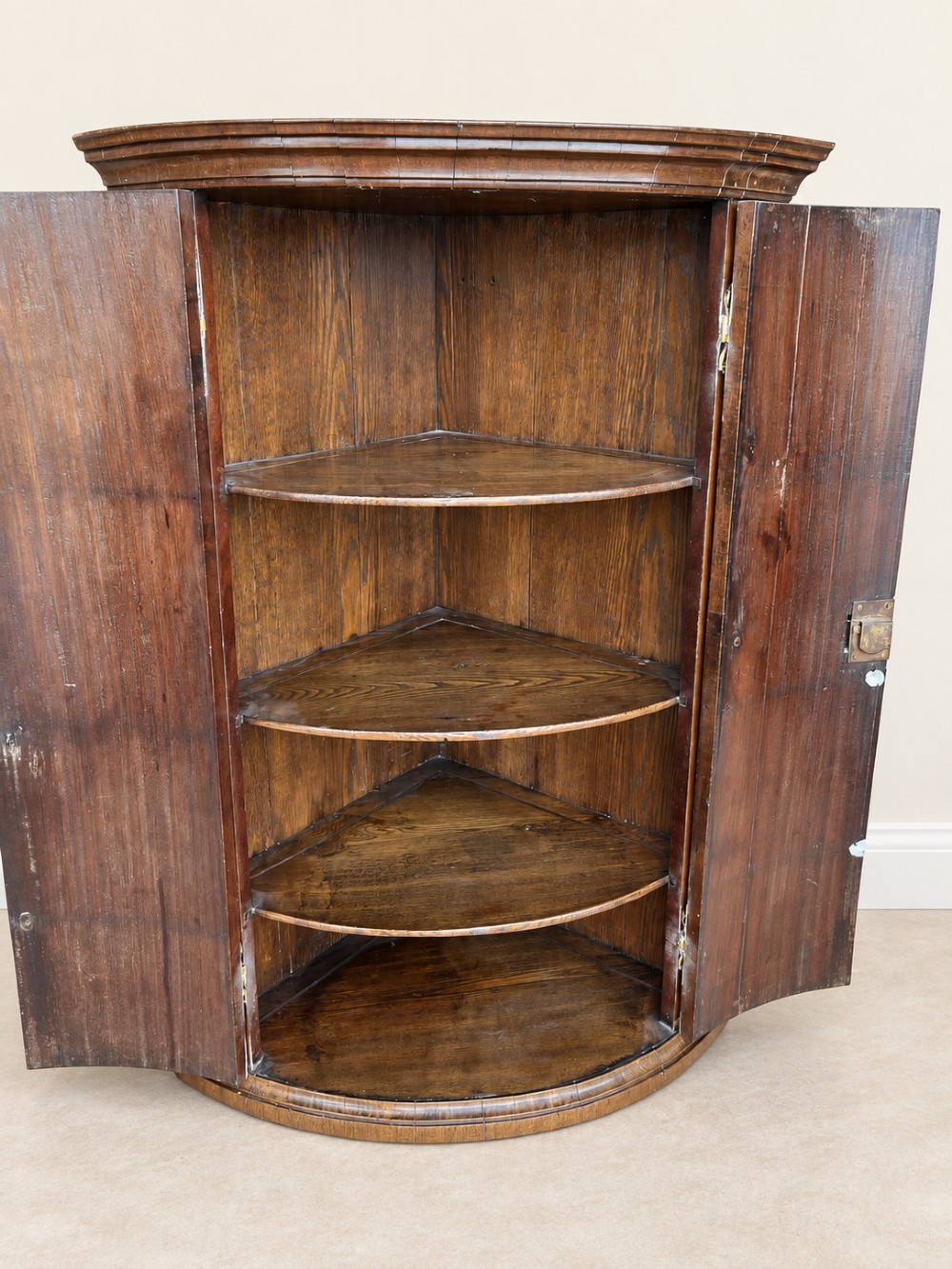 An antique Georgian mahogany corner cupboard featuring a curved bowfront double-door structure with ornate brass hinges and moulding. View IX
