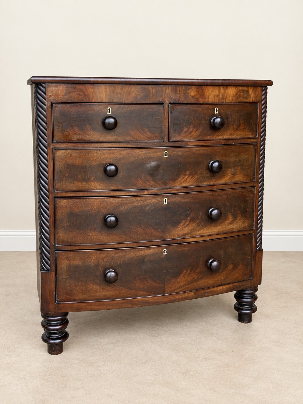 A 19th-century mahogany bowfront chest of drawers featuring spiral rope-twist pilasters, turned wooden knobs, and brass keyhole escutcheons.