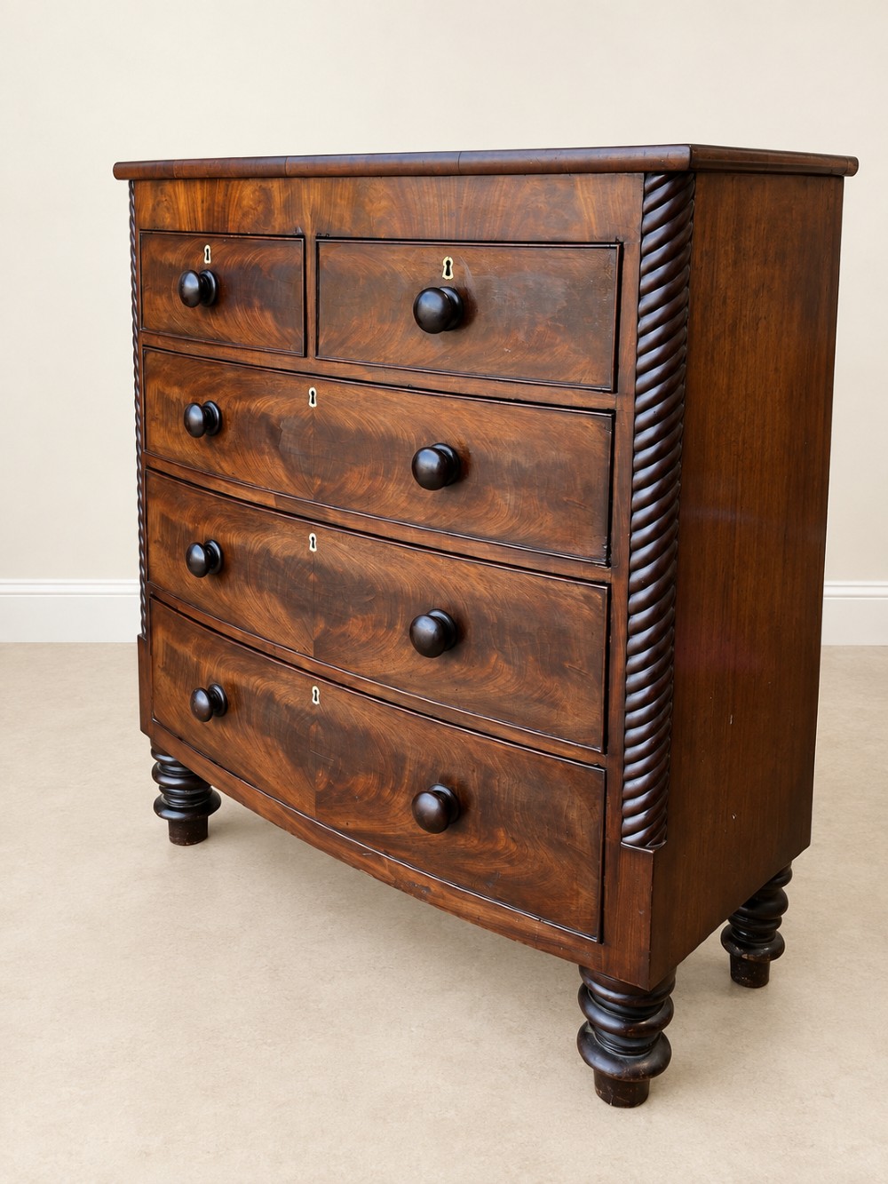 A 19th-century mahogany bowfront chest of drawers featuring spiral rope-twist pilasters, turned wooden knobs, and brass keyhole escutcheons. View II
