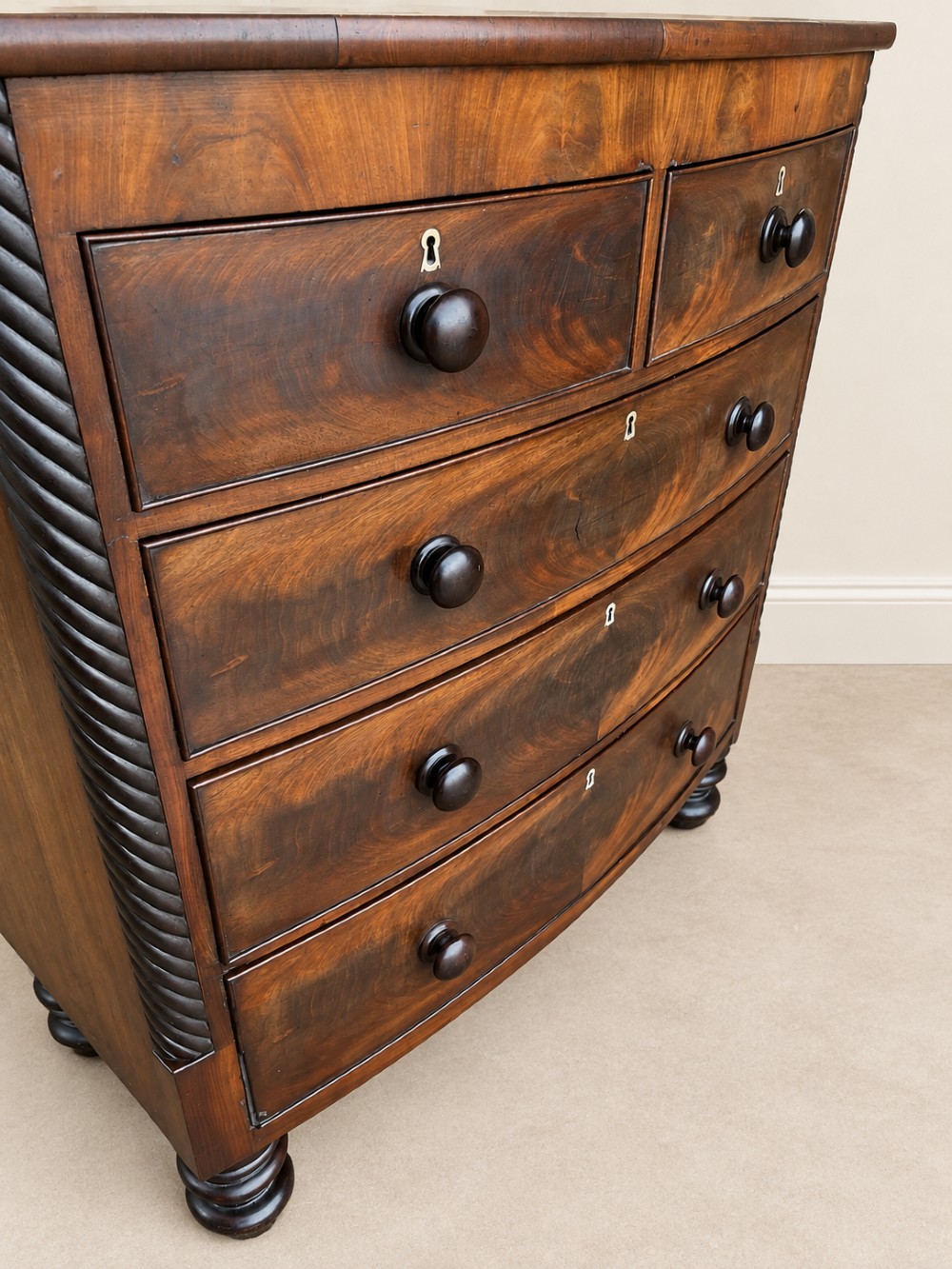A 19th-century mahogany bowfront chest of drawers featuring spiral rope-twist pilasters, turned wooden knobs, and brass keyhole escutcheons. View VI