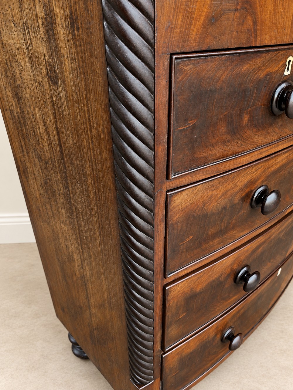 A 19th-century mahogany bowfront chest of drawers featuring spiral rope-twist pilasters, turned wooden knobs, and brass keyhole escutcheons. View VII
