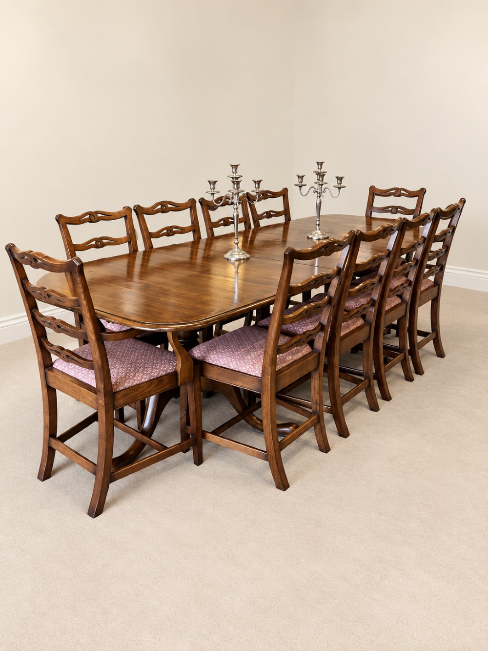A large extendable mahogany dining table surrounded by ten matching wooden chairs with patterned pink fabric seats.