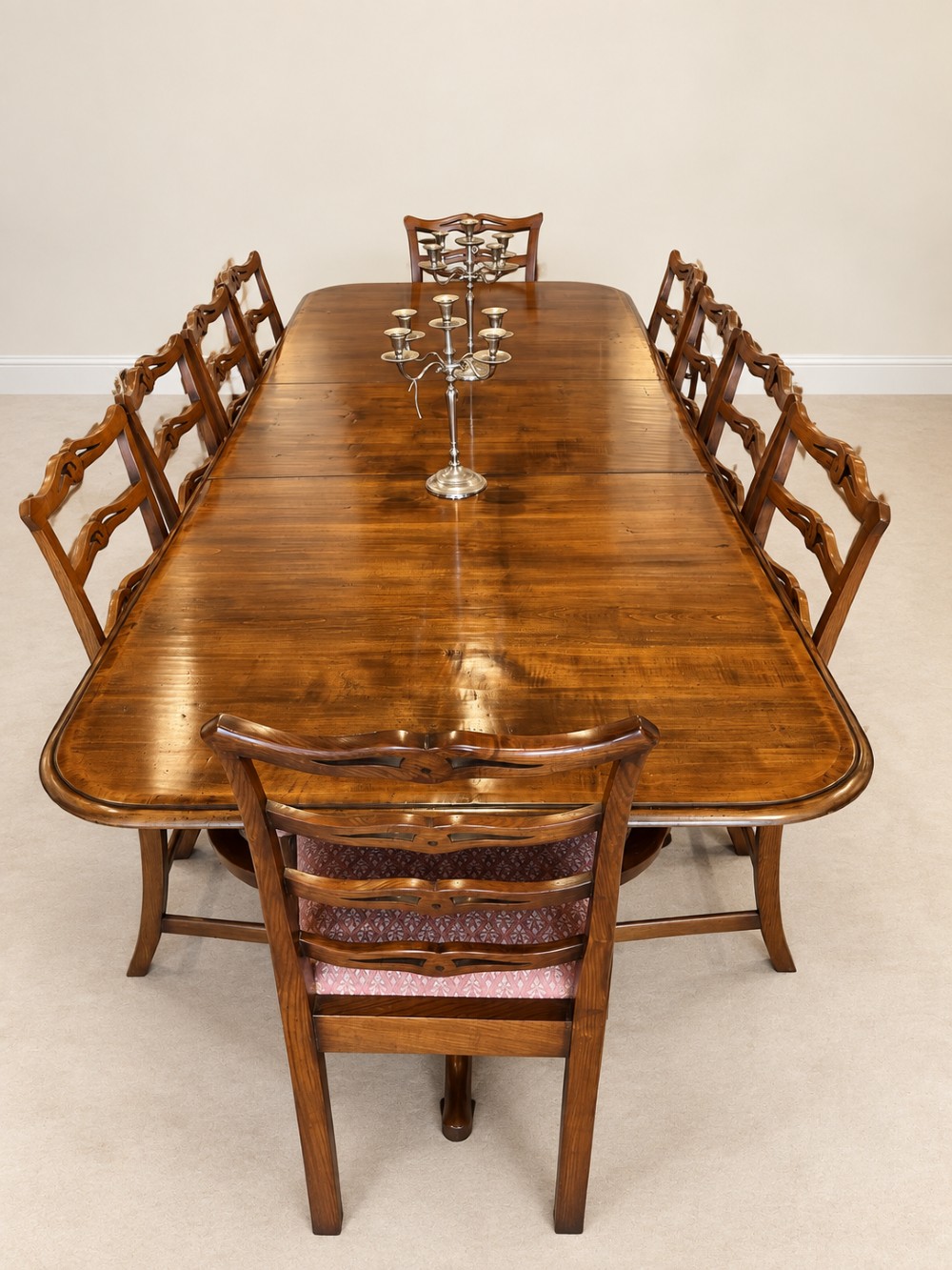A large extendable mahogany dining table surrounded by ten matching wooden chairs with patterned pink fabric seats. View II