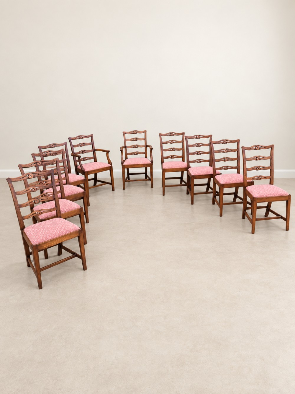 A large extendable mahogany dining table surrounded by ten matching wooden chairs with patterned pink fabric seats. View VI
