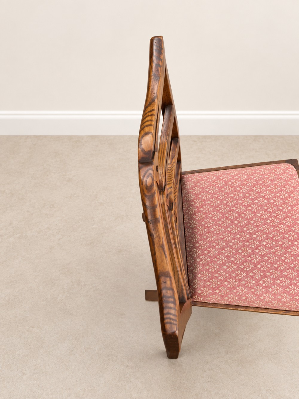 A large extendable mahogany dining table surrounded by ten matching wooden chairs with patterned pink fabric seats. View X