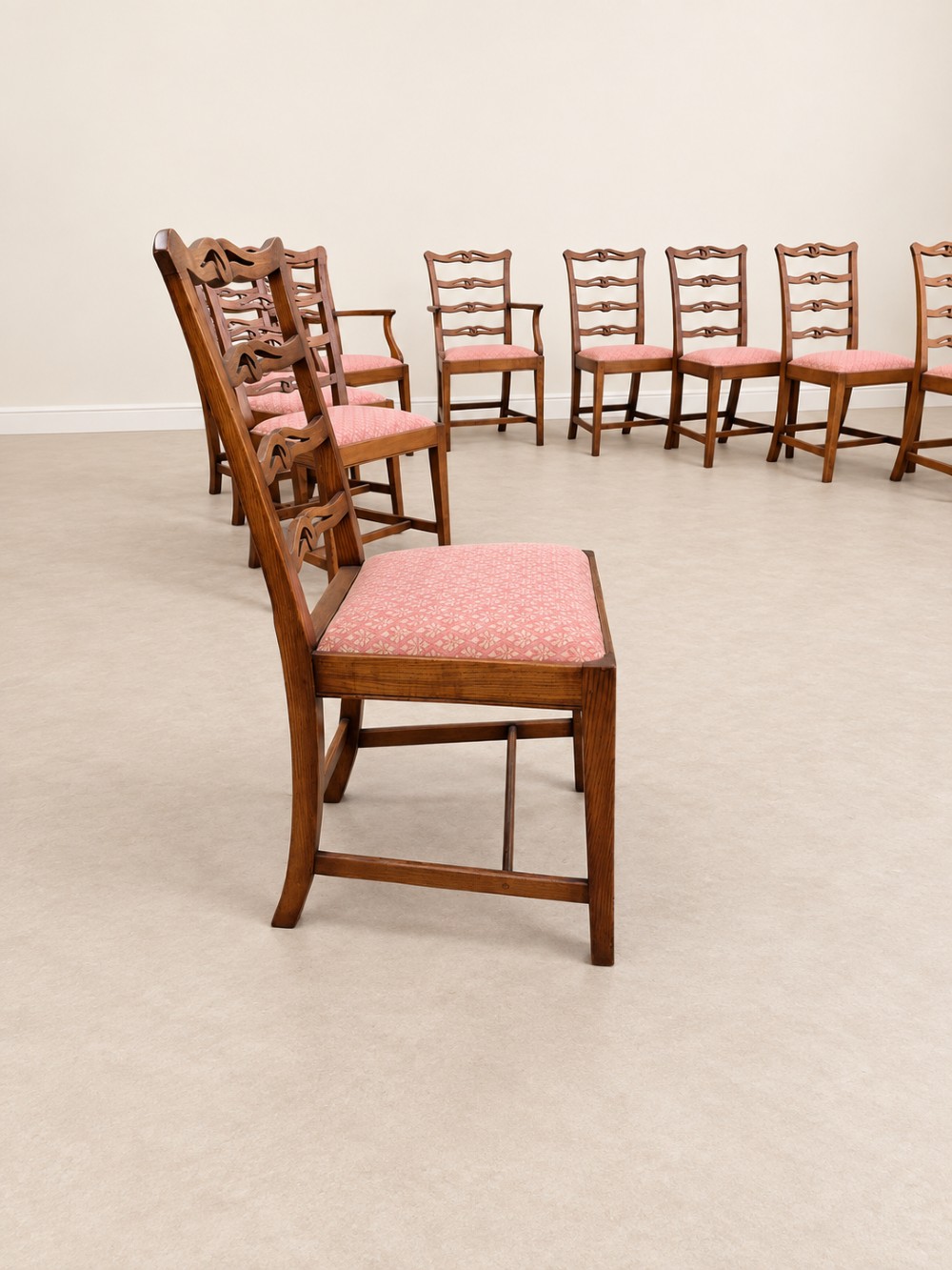 A large extendable mahogany dining table surrounded by ten matching wooden chairs with patterned pink fabric seats. View XII