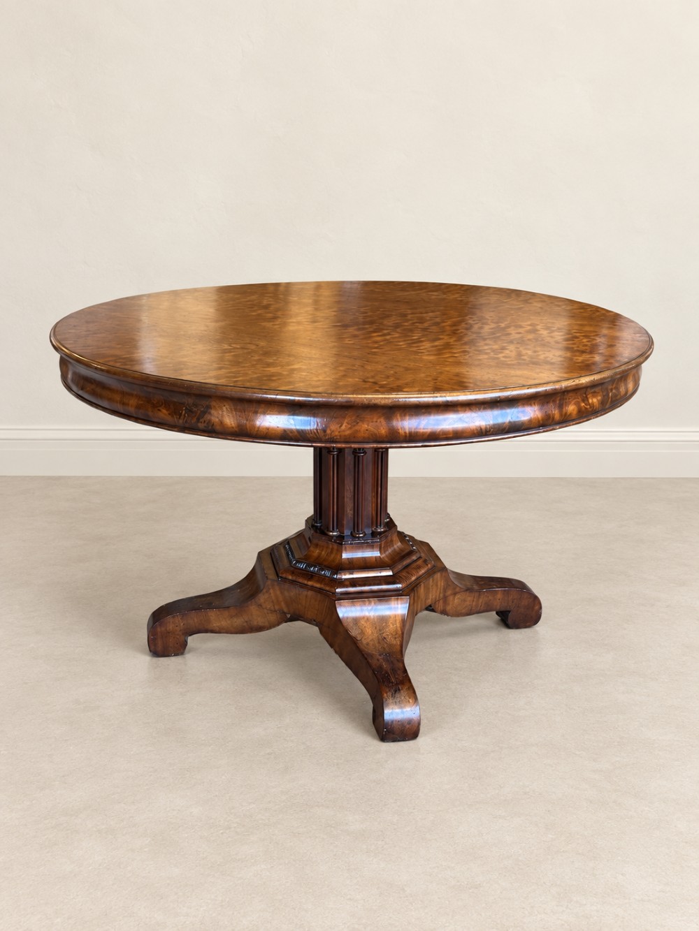 A 19th-century circular mahogany dining table featuring a figured grain top, fluted central pedestal column, and a quadform platform base on scroll feet.