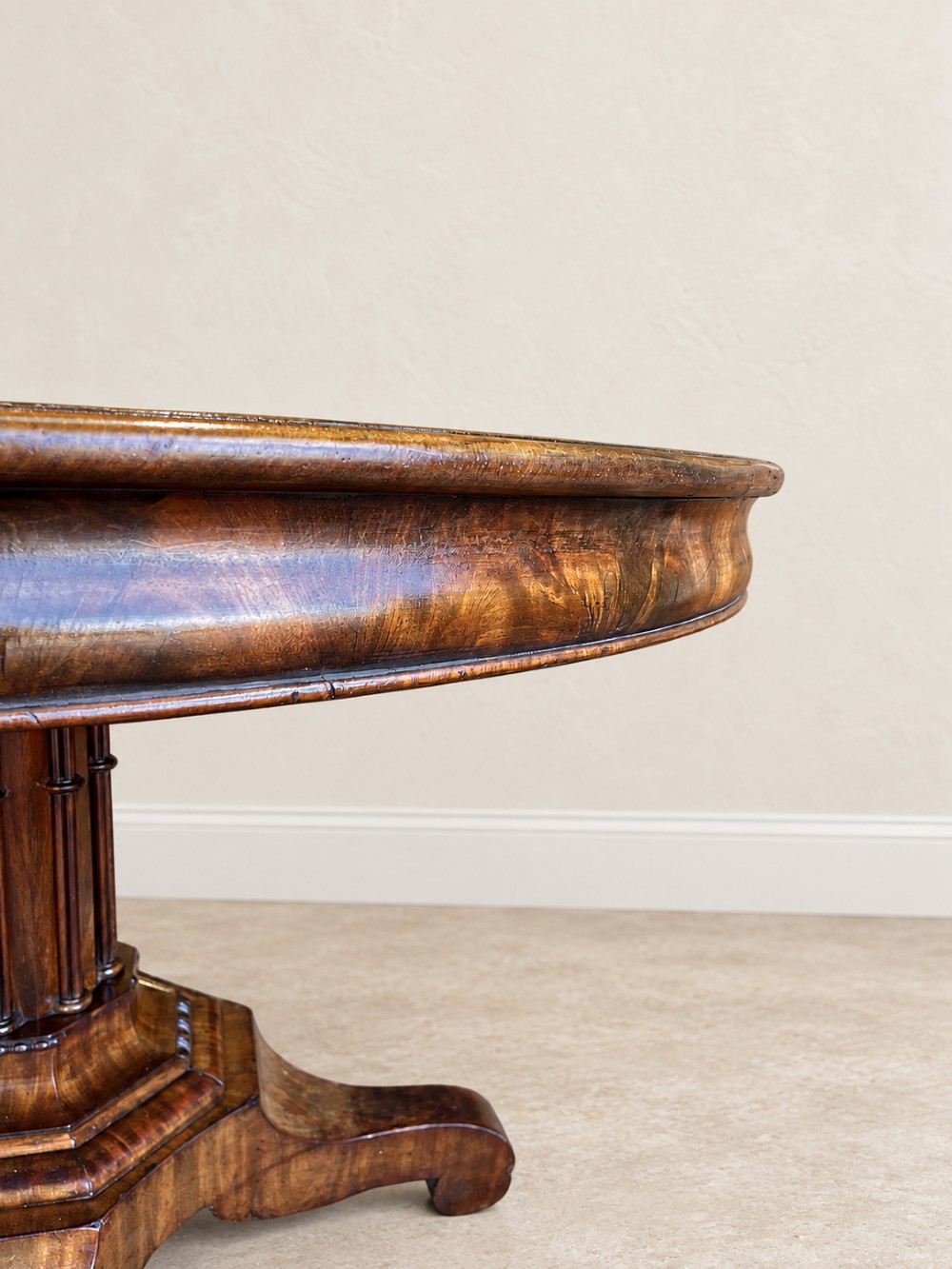 A 19th-century circular mahogany dining table featuring a figured grain top, fluted central pedestal column, and a quadform platform base on scroll feet. View IV