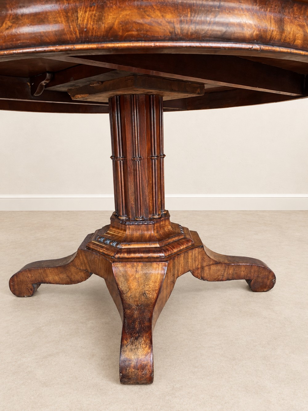 A 19th-century circular mahogany dining table featuring a figured grain top, fluted central pedestal column, and a quadform platform base on scroll feet. View VI