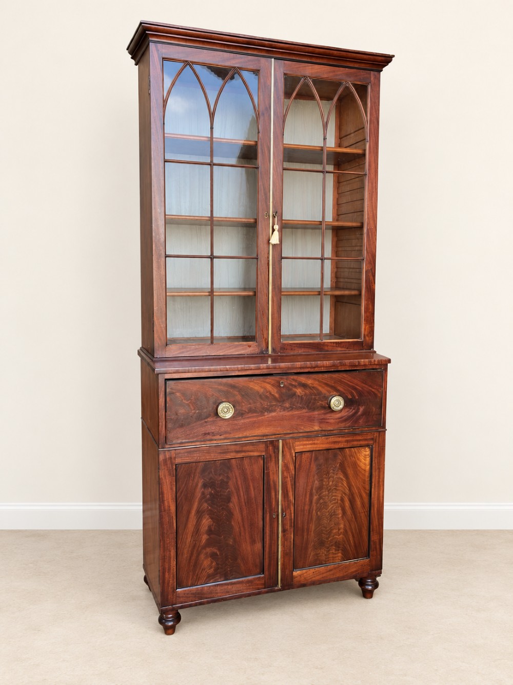A tall 19th-century mahogany secretaire bookcase featuring upper glazed doors with Gothic arched astragal glazing, a deep drawer, and a lower two-door cupboard standing on turned feet.
