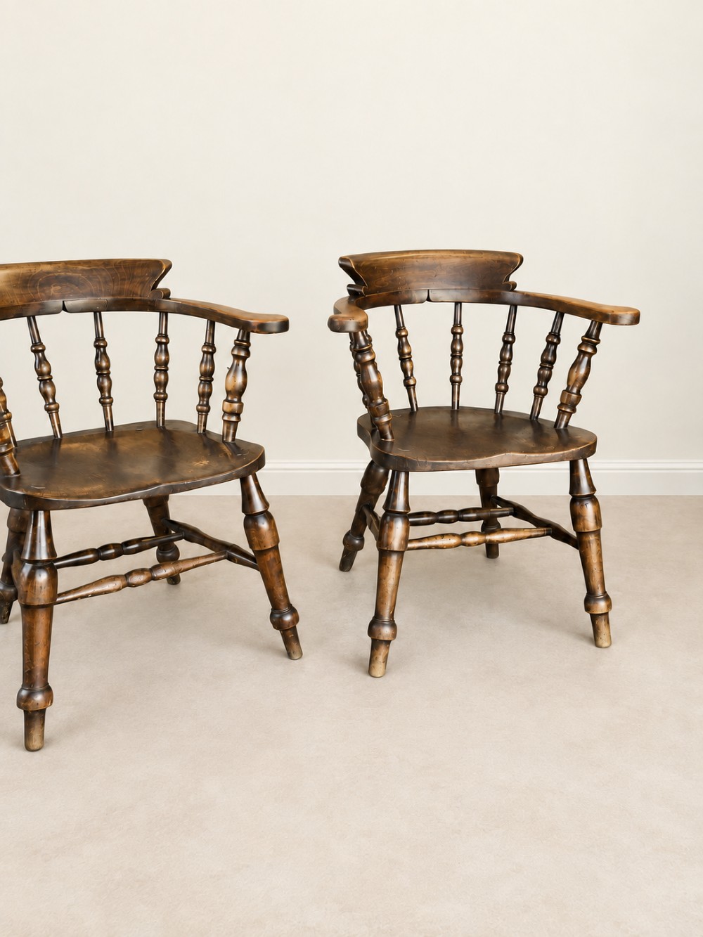 A pair of 19th-century dark wood captains chairs featuring turned spindles, contoured saddle seats, and turned legs joined by stretchers. View V