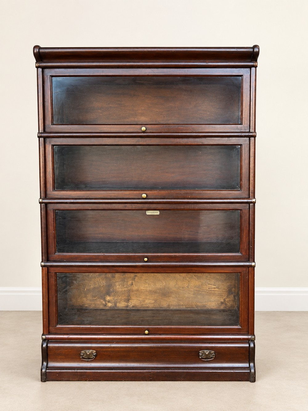 A four-tier dark mahogany Globe Wernicke sectional bookcase featuring glazed lift-up doors and a bottom drawer with brass handles.