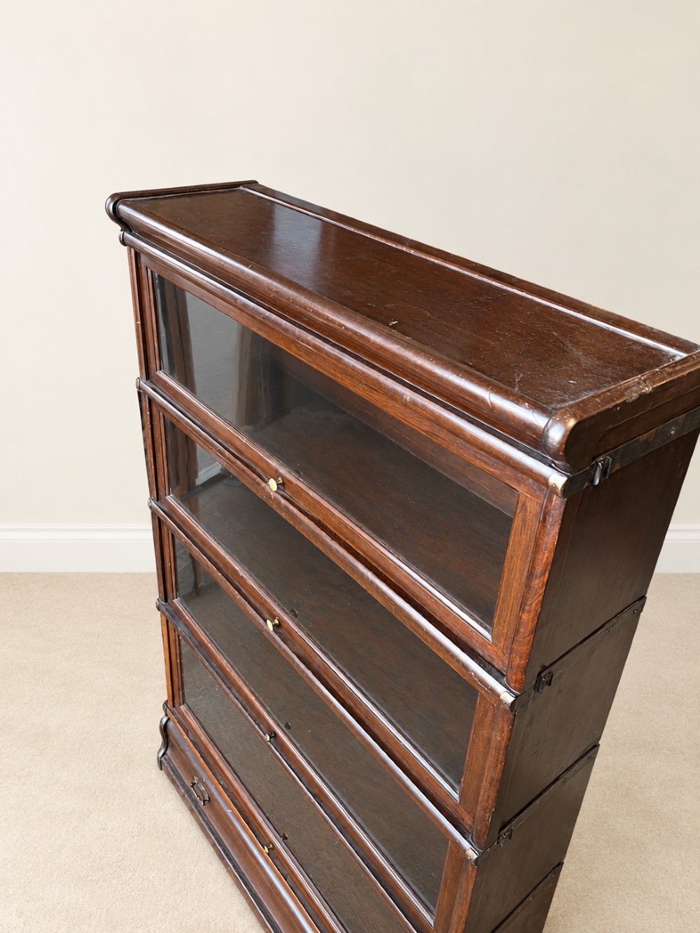 A four-tier dark mahogany Globe Wernicke sectional bookcase featuring glazed lift-up doors and a bottom drawer with brass handles. View IV