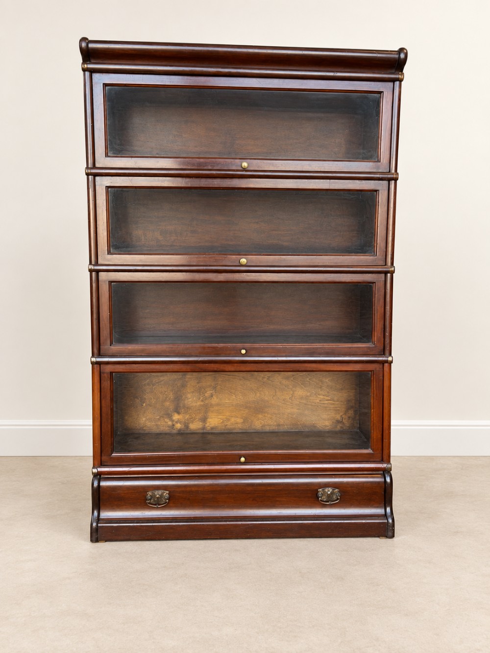 A four-tier dark mahogany Globe Wernicke sectional bookcase featuring glazed lift-up doors and a bottom drawer with brass handles. View V