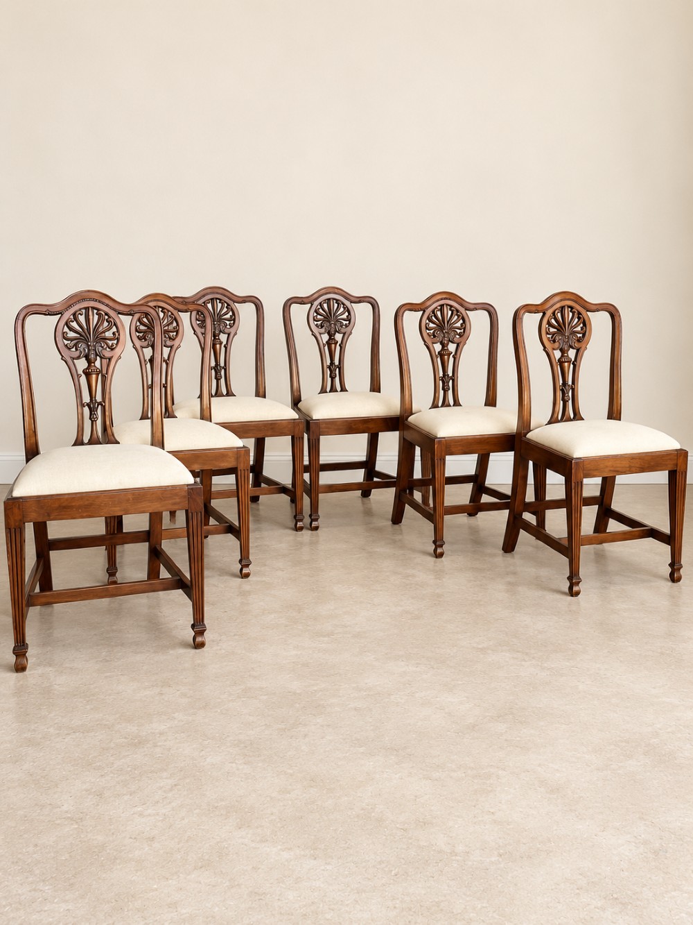 A set of six mahogany dining chairs featuring intricate carved splat backs and neutral cream fabric seats.