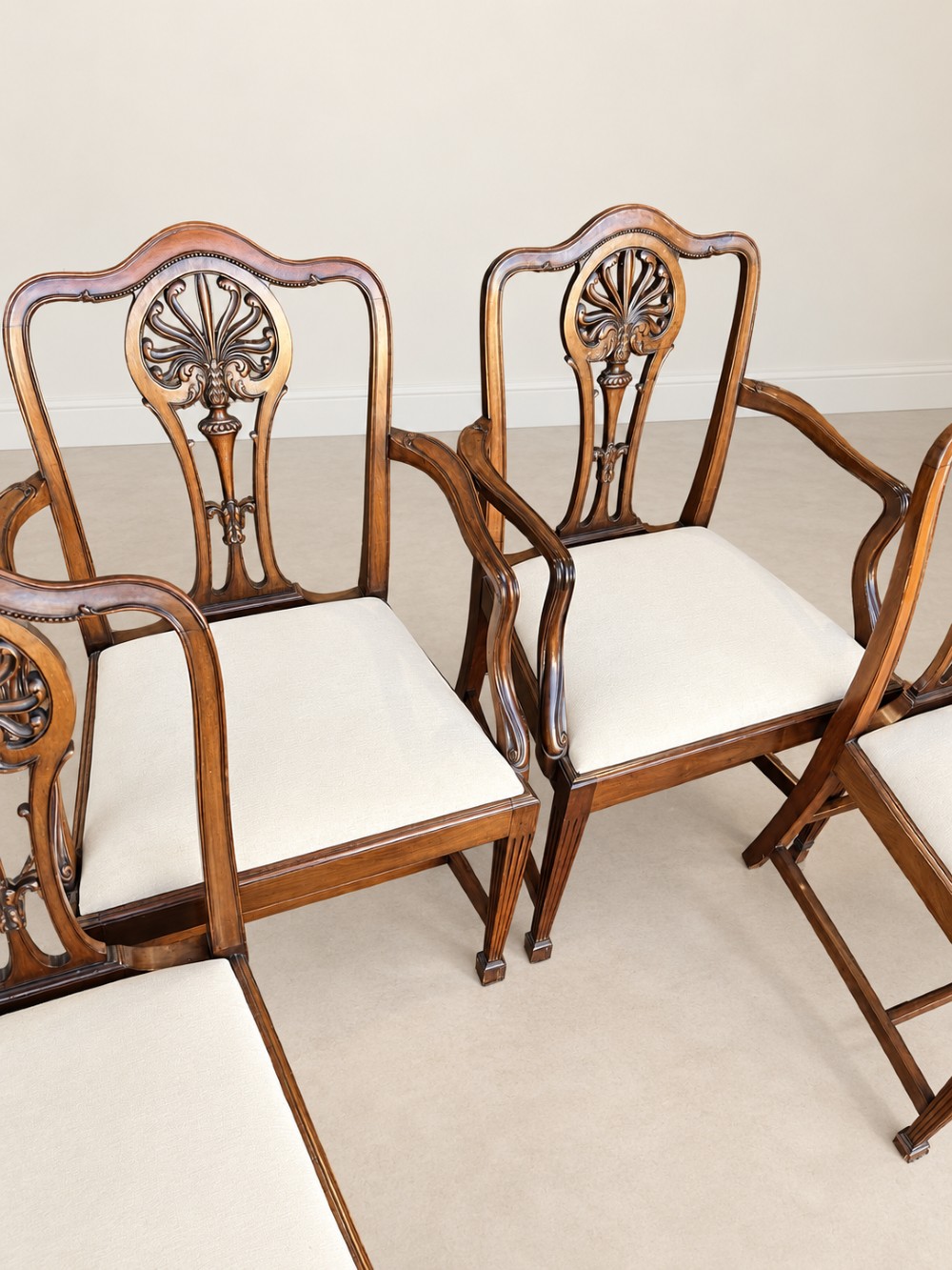 A set of six mahogany dining chairs featuring intricate carved splat backs and neutral cream fabric seats. View III