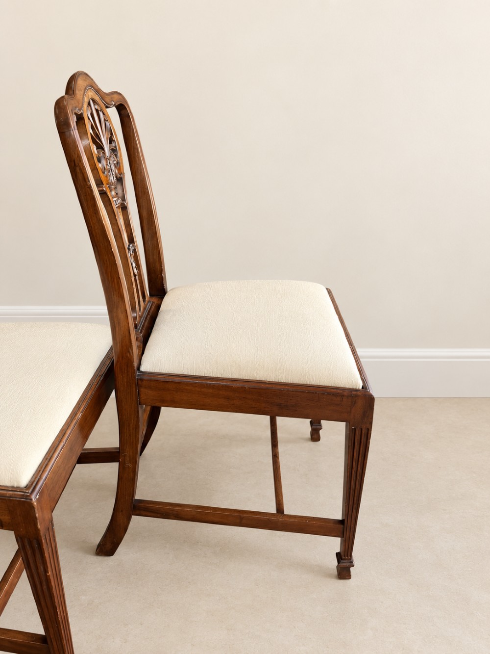 A set of six mahogany dining chairs featuring intricate carved splat backs and neutral cream fabric seats. View V