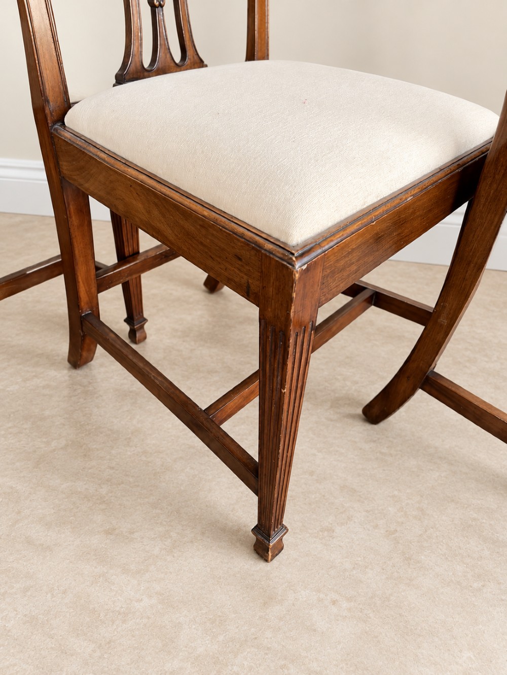 A set of six mahogany dining chairs featuring intricate carved splat backs and neutral cream fabric seats. View VI