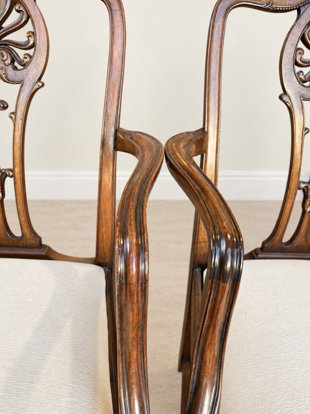 A set of six mahogany dining chairs featuring intricate carved splat backs and neutral cream fabric seats. View VII