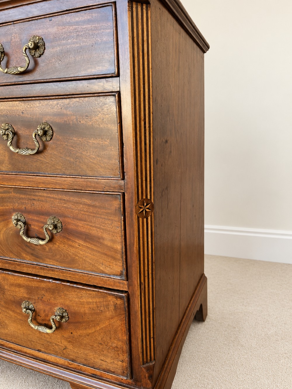 An antique George III mahogany chest of drawers featuring two short over three long drawers with decorative brass swan-neck handles and bracket feet. View III