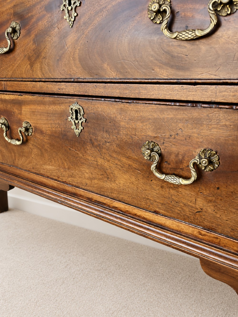 An antique George III mahogany chest of drawers featuring two short over three long drawers with decorative brass swan-neck handles and bracket feet. View V