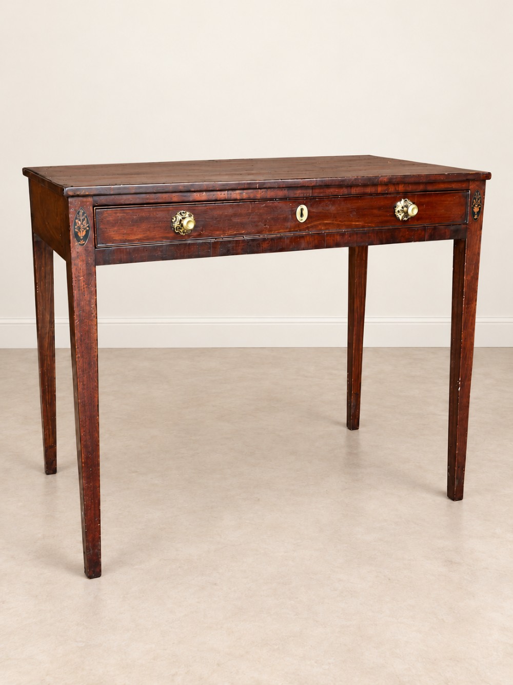 An antique nineteenth-century mahogany side table featuring a single drawer, brass handles, decorative oval floral inlay, and slender tapered legs.