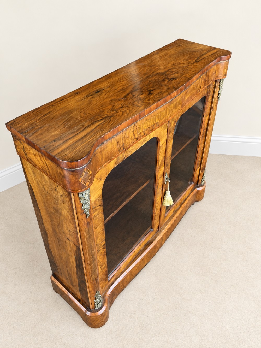 A 19th-century burr walnut low bookcase featuring two glazed doors, a serpentine front profile, geometric marquetry inlay, and decorative brass mounts. View III