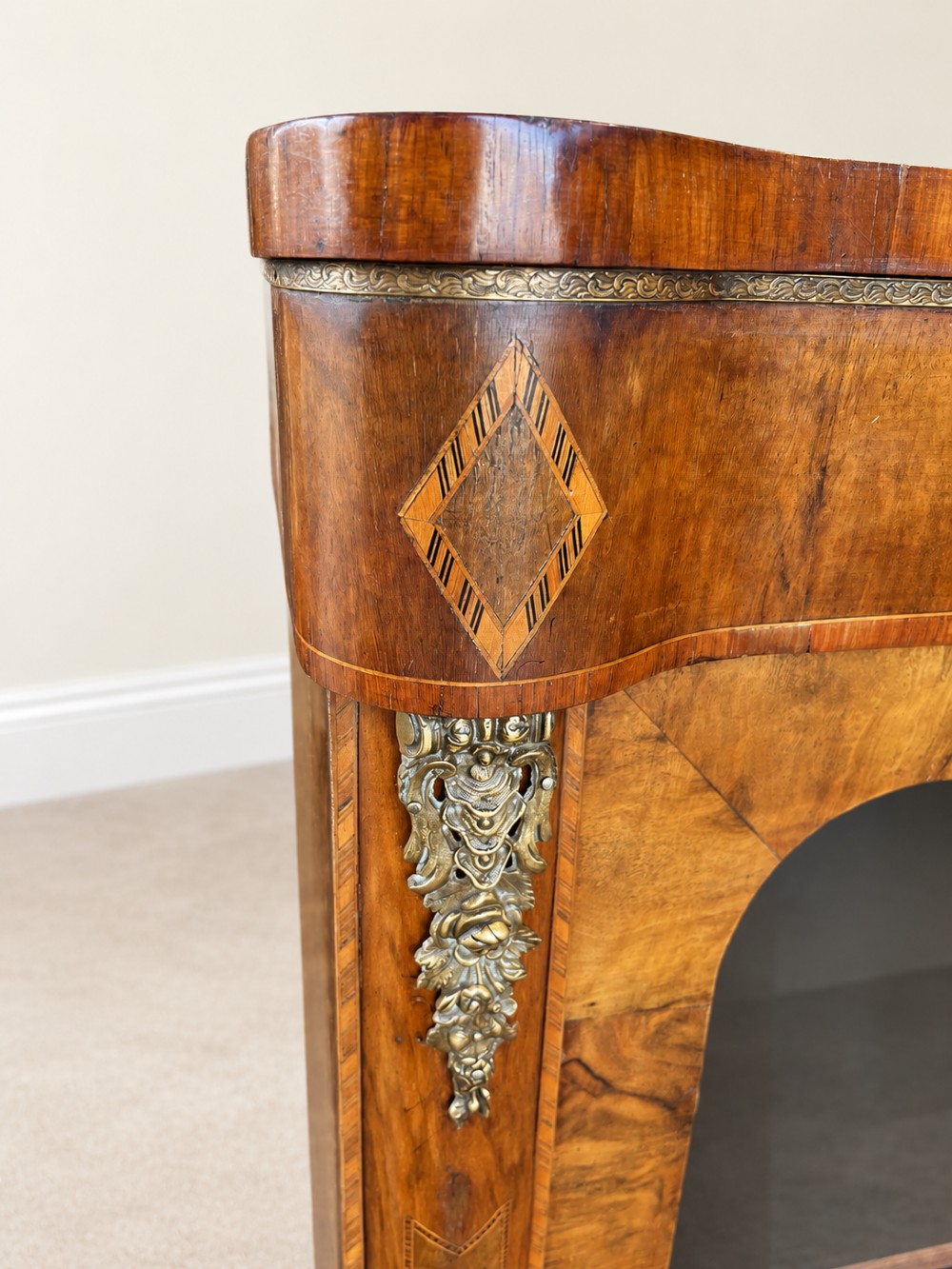 A 19th-century burr walnut low bookcase featuring two glazed doors, a serpentine front profile, geometric marquetry inlay, and decorative brass mounts. View IV
