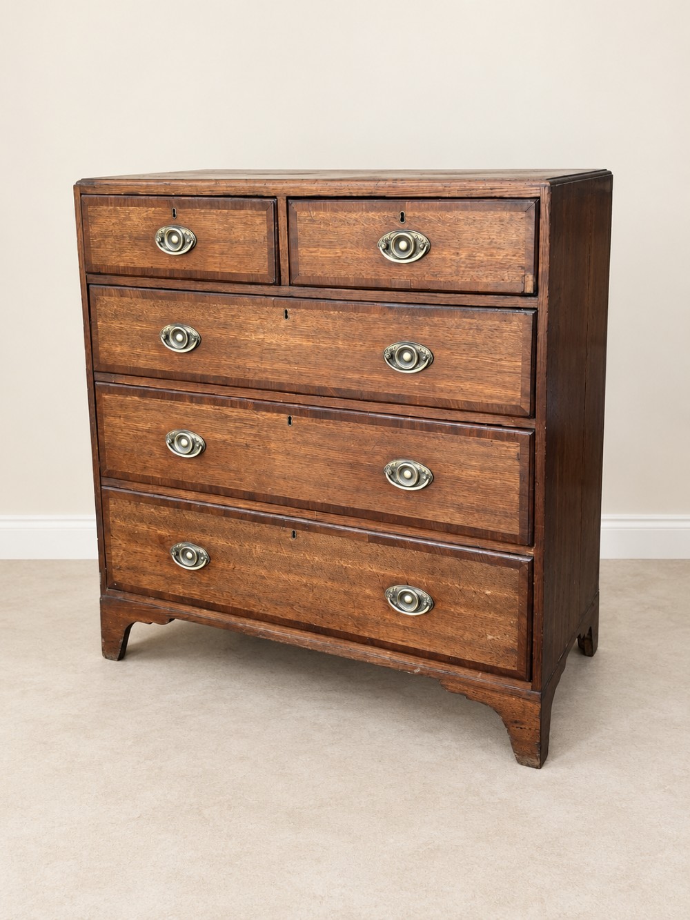 An antique Georgian oak chest of drawers featuring two short drawers above three long drawers with oval brass handles and bracket feet.