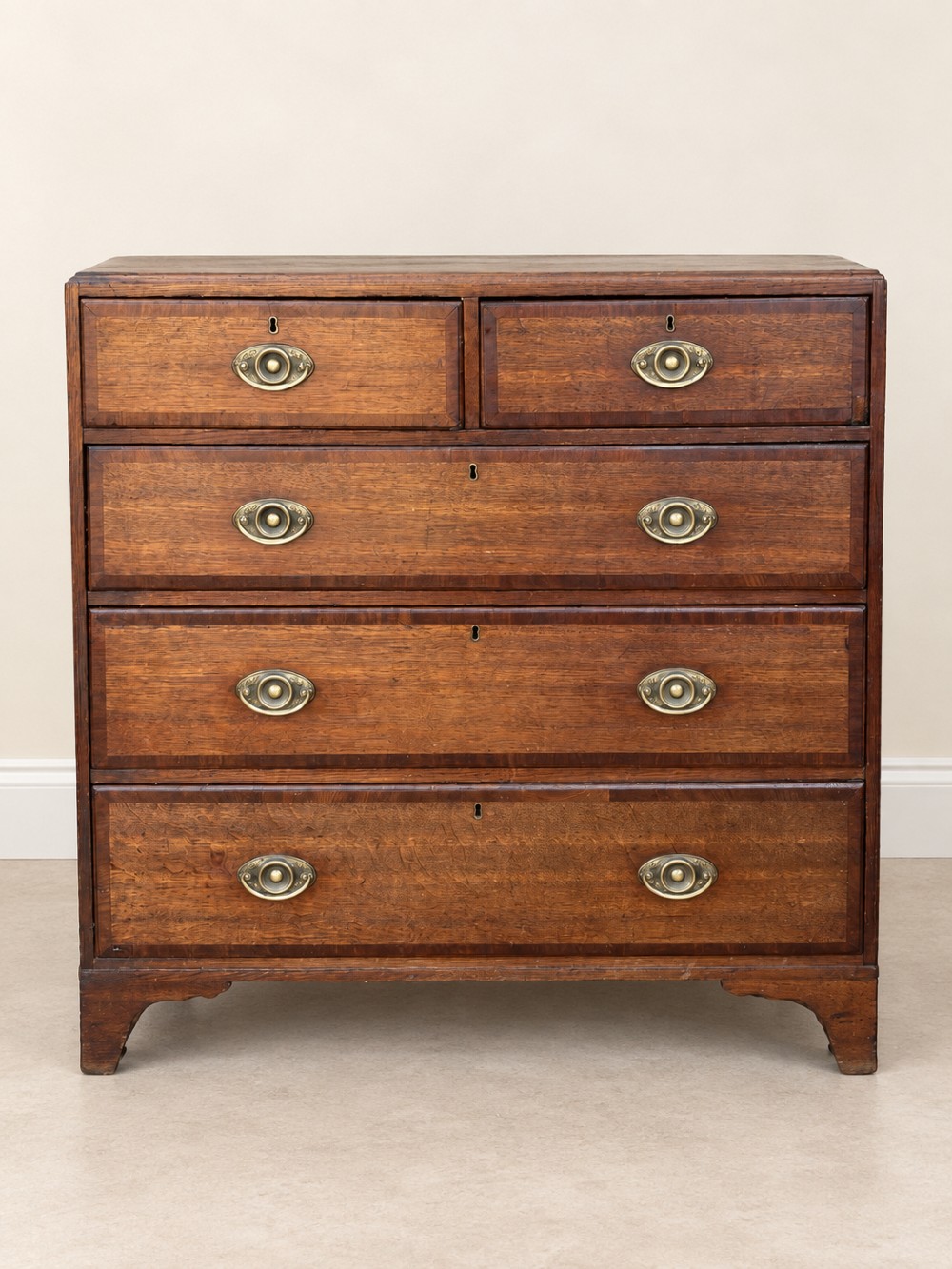 An antique Georgian oak chest of drawers featuring two short drawers above three long drawers with oval brass handles and bracket feet. View III