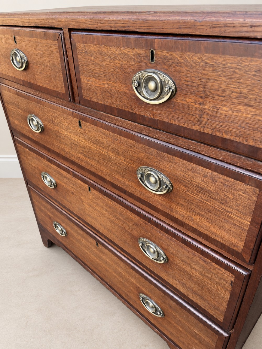 An antique Georgian oak chest of drawers featuring two short drawers above three long drawers with oval brass handles and bracket feet. View IV