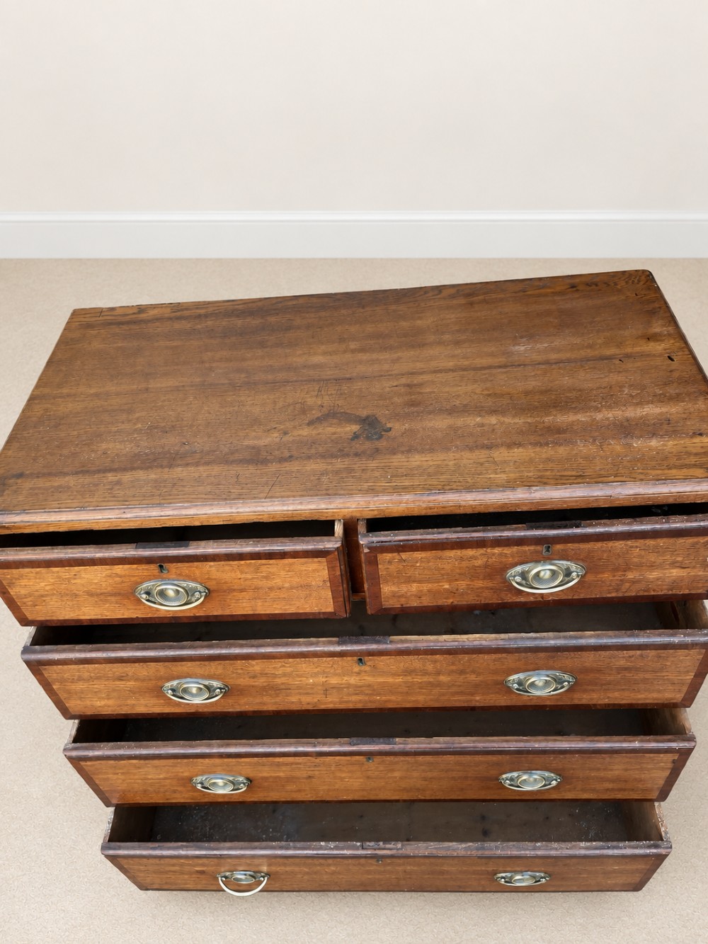 An antique Georgian oak chest of drawers featuring two short drawers above three long drawers with oval brass handles and bracket feet. View V