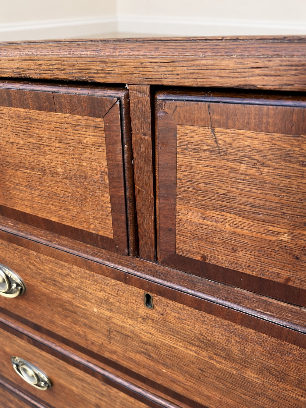 An antique Georgian oak chest of drawers featuring two short drawers above three long drawers with oval brass handles and bracket feet. View VI
