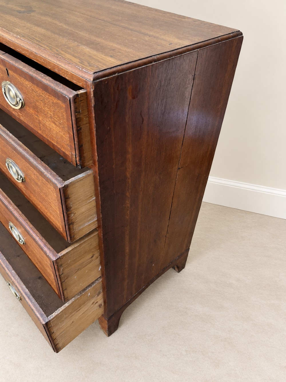 An antique Georgian oak chest of drawers featuring two short drawers above three long drawers with oval brass handles and bracket feet. View VII