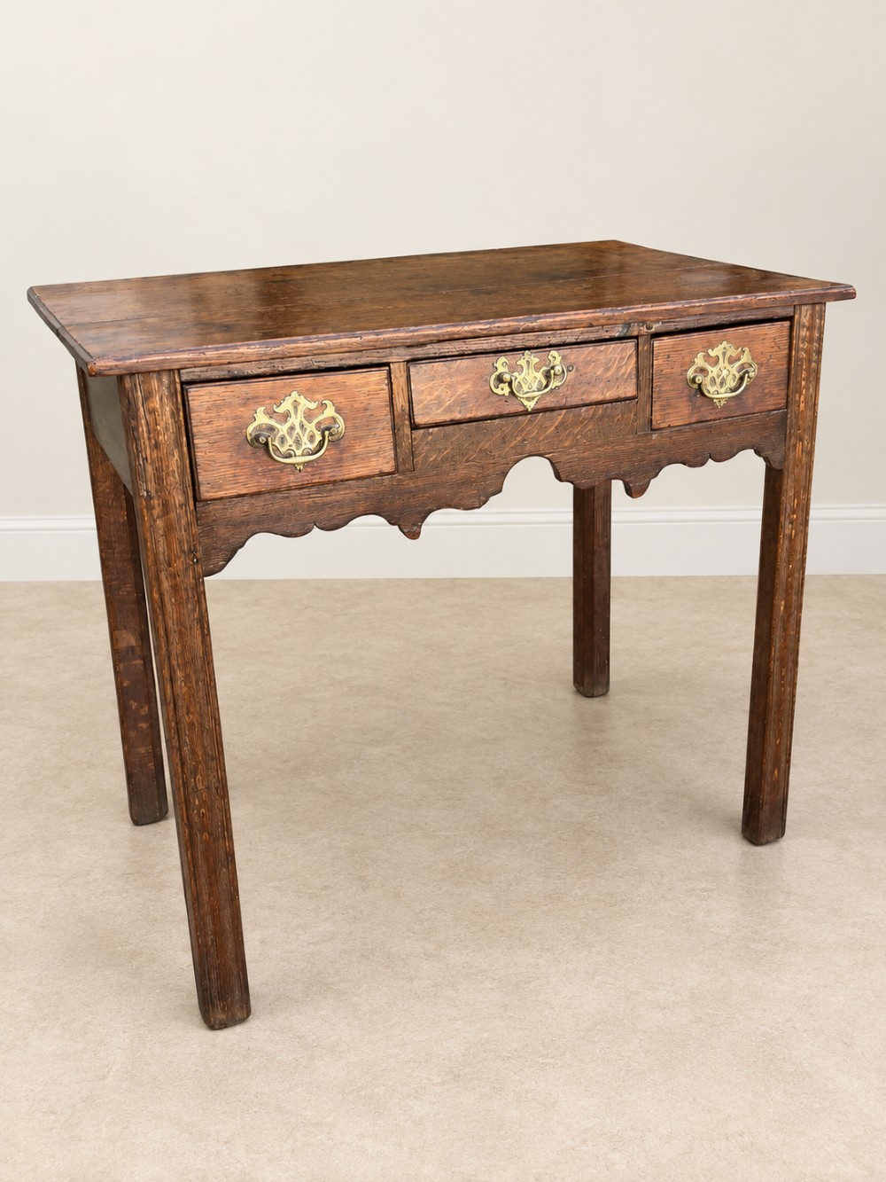 An 18th-century dark oak lowboy side table featuring three drawers with brass handles and a scalloped apron. View II