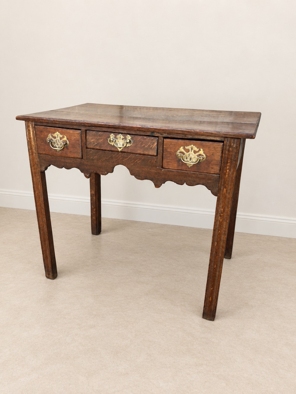 An 18th-century dark oak lowboy side table featuring three drawers with brass handles and a scalloped apron. View III