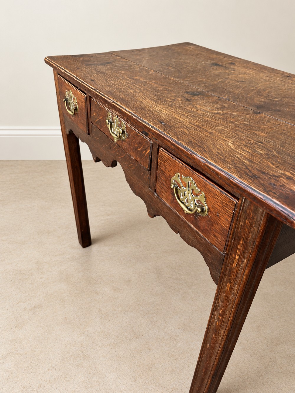 An 18th-century dark oak lowboy side table featuring three drawers with brass handles and a scalloped apron. View VI